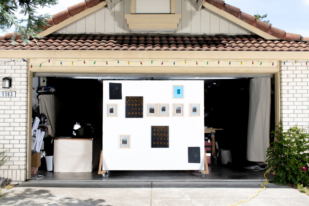 A suburban garage with an open garage door, framing a large wall with various framed artworks.